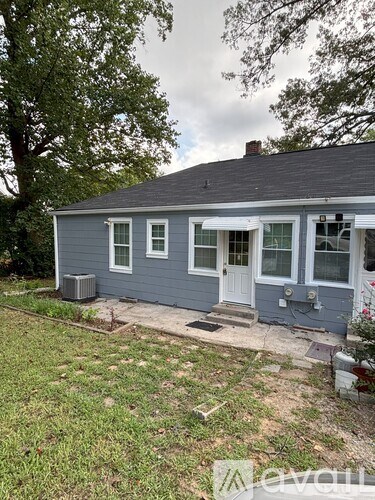 A small house with a white door and windows is surrounded by a grassy area.