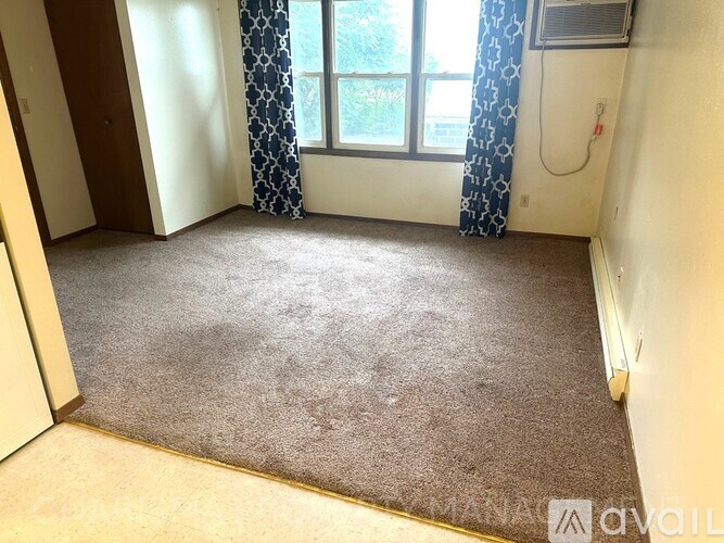 A room with a carpeted floor and a window with curtains.