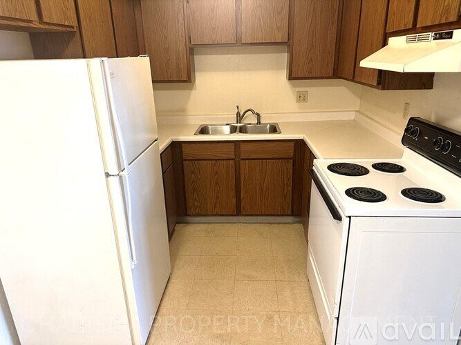 A kitchen with a white refrigerator, white stove, and wooden cabinets.