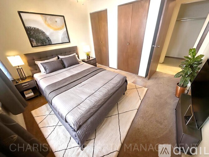 A bedroom with a large bed, a nightstand with a lamp, and a painting on the wall.