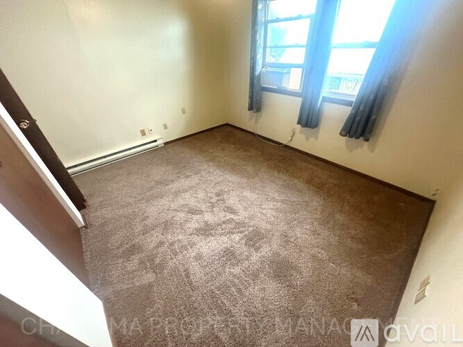 A room with a carpeted floor and a window with black curtains.