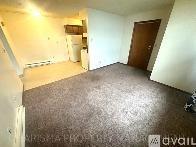 A spacious room with a brown carpet and white walls, containing a white refrigerator and a brown door.