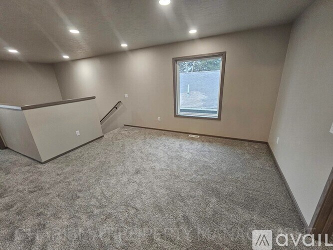 A room with a grey carpet and a window with a view of a building outside.