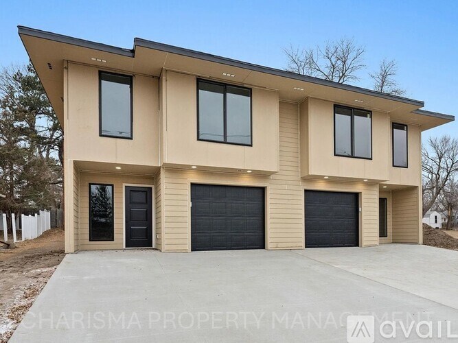 A modern house with a beige facade and black garage doors is for sale.