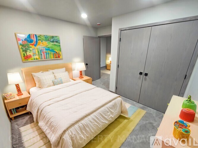 A bedroom with a large bed, a nightstand with two lamps, a painting on the wall, and a wardrobe.