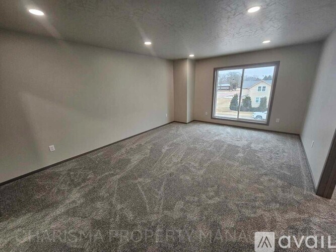 A room with a carpeted floor and a window showing a residential area outside.