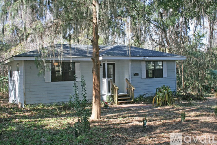 A small house with a porch and a tree in front.
