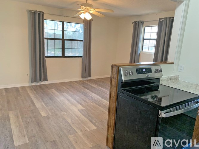 A kitchen with a wood floor, a stove, and a window with curtains.