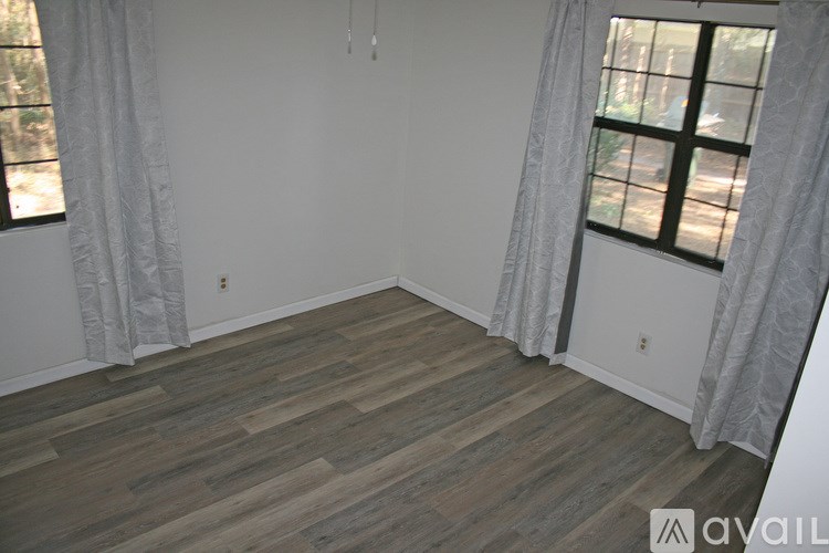 A room with wooden flooring and a window with white curtains.