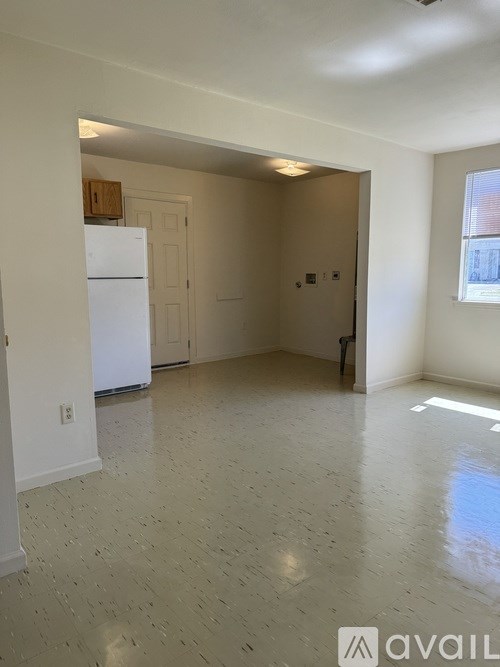 A spacious room with a white refrigerator and a doorway leading to another room.