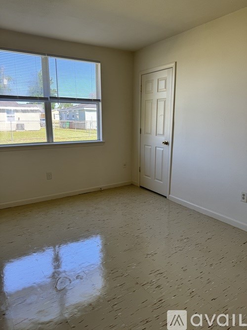 A room with a door and a window with a view of a fence and a building outside.