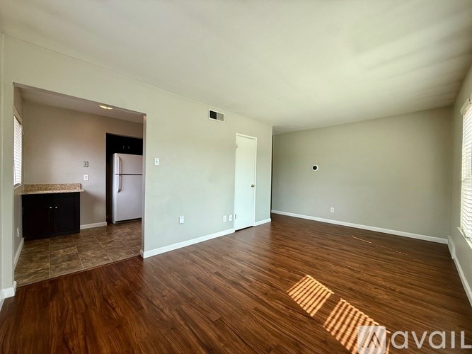 A room with wooden floors and a kitchen area in the background.