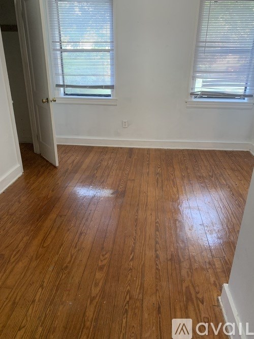 A room with wooden flooring and two windows with blinds.