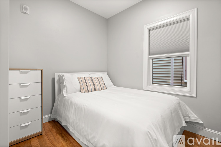 A white bed with a pillow and a window with blinds.