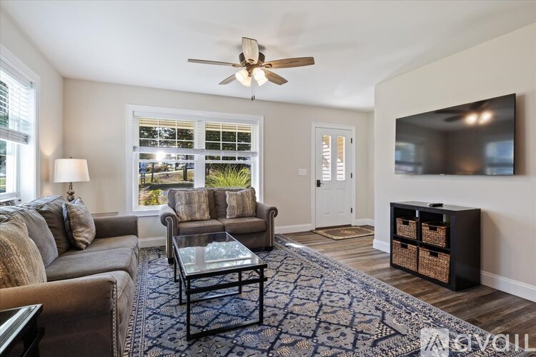 A living room with a grey couch, a glass coffee table, and a flat screen TV mounted on the wall.