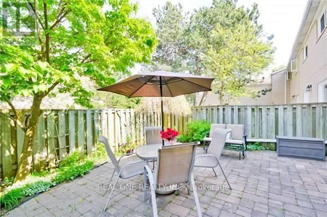 A patio with a table, chairs, and an umbrella is surrounded by a wooden fence and trees.