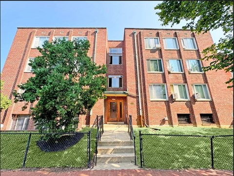 A red brick building with a black fence and a tree in front.