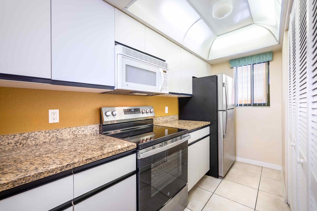 A kitchen with a black refrigerator, white cabinets, and a granite countertop.