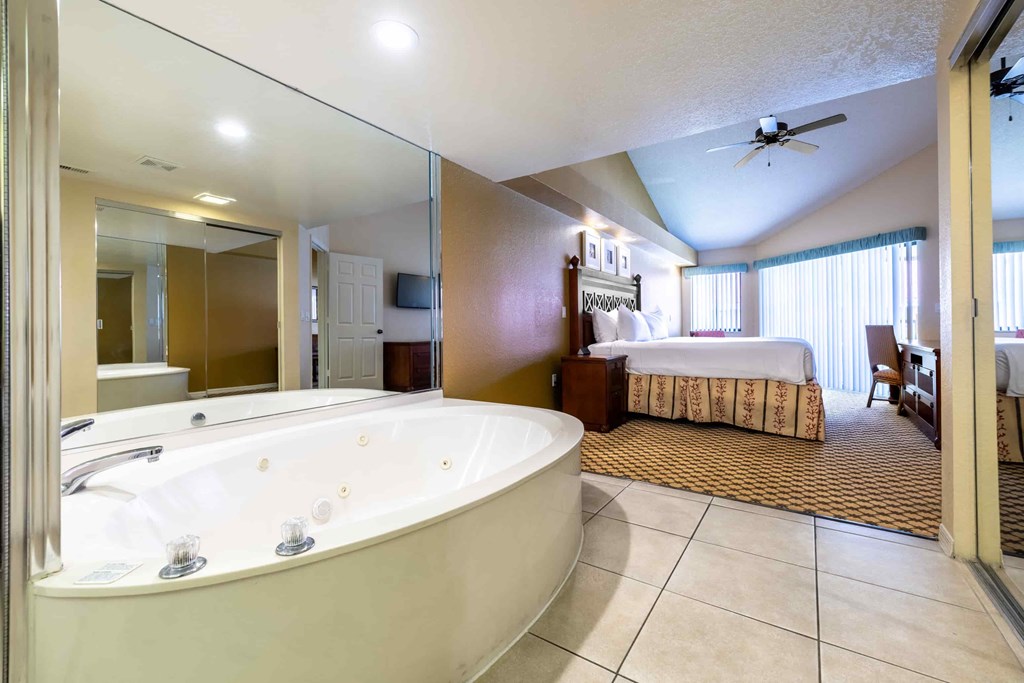 A large, white bathtub is in a spacious bathroom with a bedroom in the background.