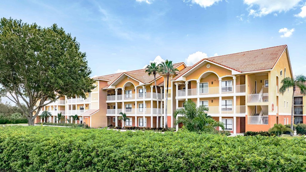 A large building with a red roof and balconies is surrounded by greenery.