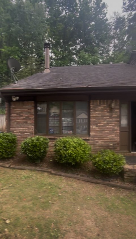 A house with a brown roof and a chimney is surrounded by green bushes.