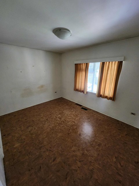 A room with a brown floor and a window with curtains.