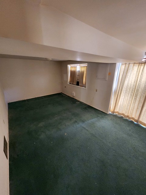 A room with a green carpet and a window with curtains.