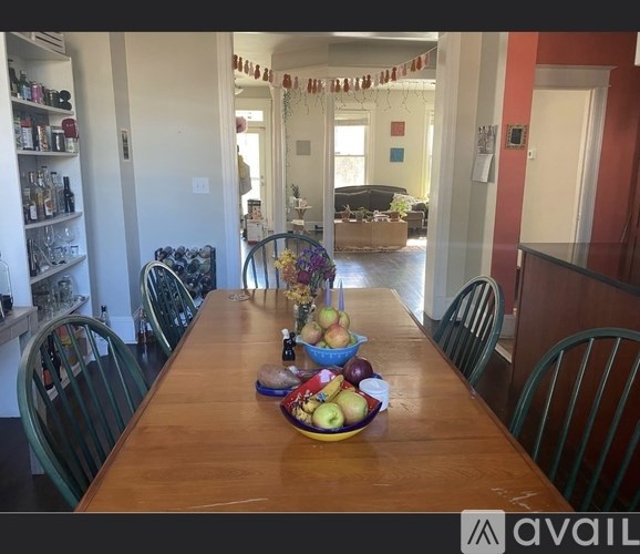 A wooden table with a bowl of fruit on it and chairs around it.
