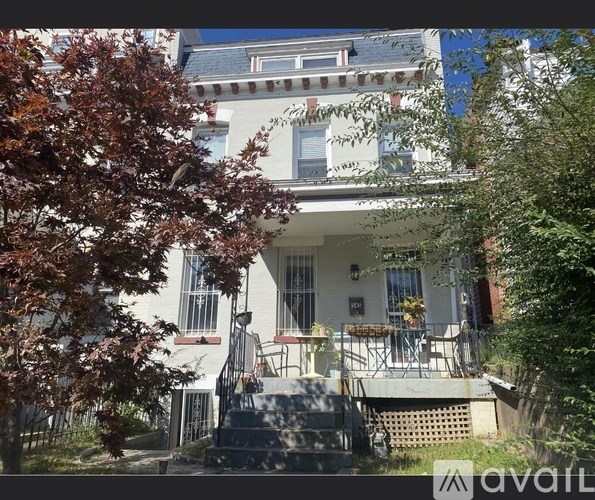 A house with a white facade and a red tree in front.