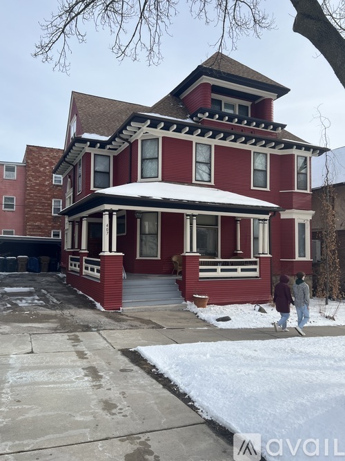 A red house with a white roof and a couple walking in front of it.