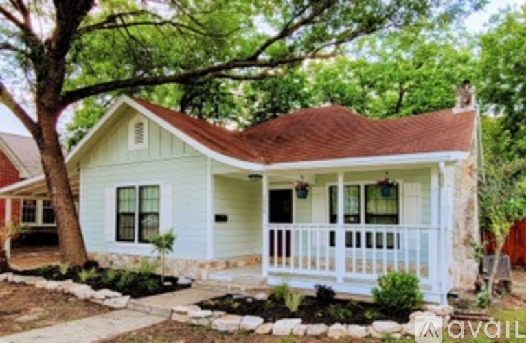 A small house with a porch and a tree in front.
