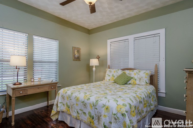 A bedroom with a bed, a desk with a lamp, and a ceiling fan.