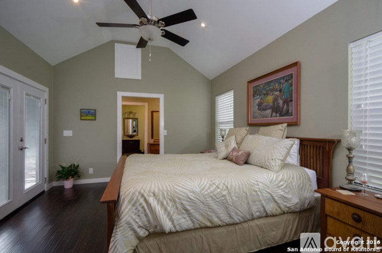A bedroom with a bed, a ceiling fan, and a painting on the wall.