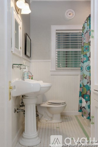 A white pedestal sink in a small bathroom with a toilet and a shower curtain.