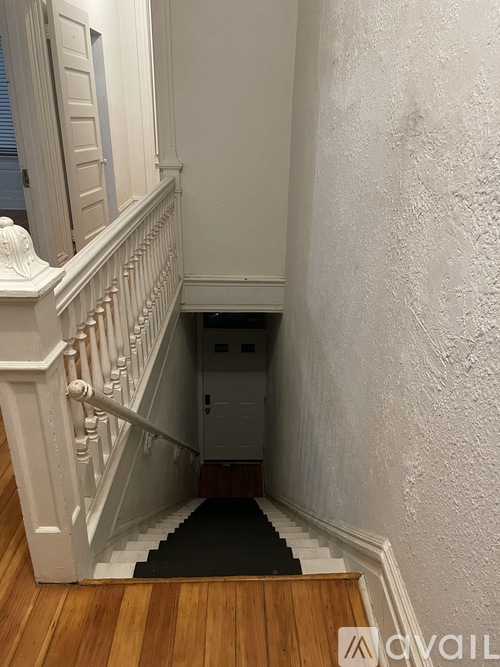 A staircase with a black carpeted step leading to a door at the bottom.