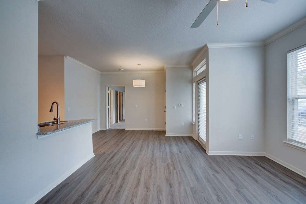 an empty living room with a kitchen and a ceiling fan