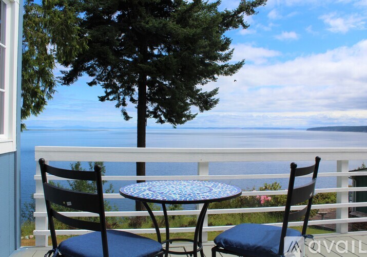 A table and two chairs are on a balcony overlooking the water.