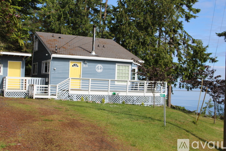 A house with a blue exterior and a yellow door is surrounded by a white fence.