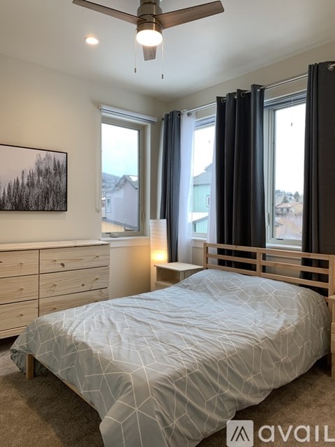 A bedroom with a bed, dresser, and window with black curtains.