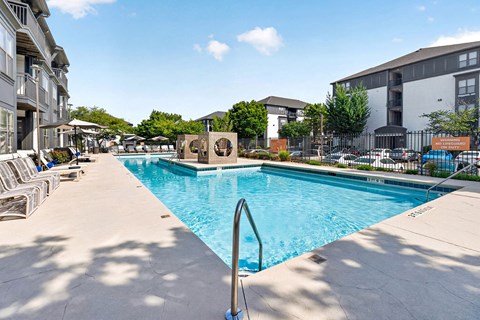 A large swimming pool surrounded by lounge chairs and buildings.