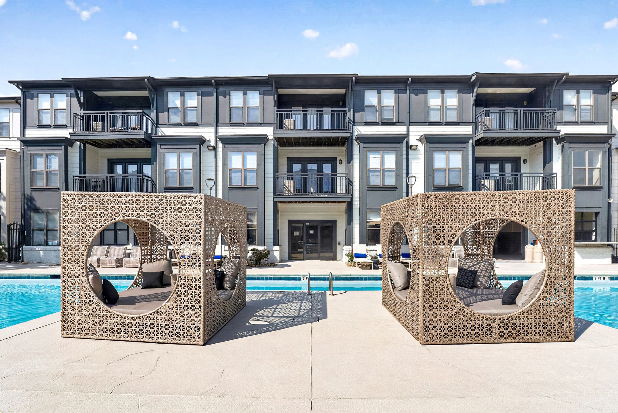 Two large cement structures with circular windows sit in front of a pool and apartment building.