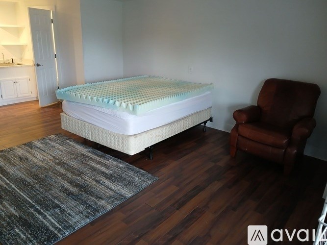 A mattress with a blue and white cover is on a wooden floor in a room with a brown leather chair.
