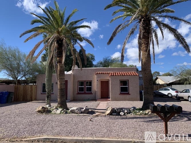 A house with a red door is surrounded by palm trees.
