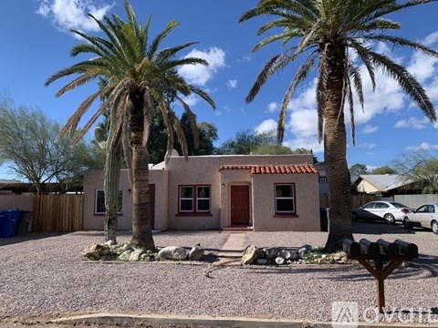 A house with a red door is surrounded by palm trees.