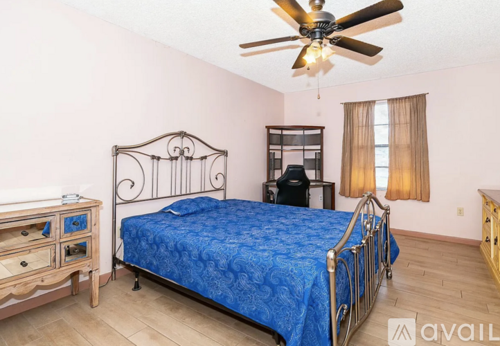 A bedroom with a blue bedspread and a ceiling fan.