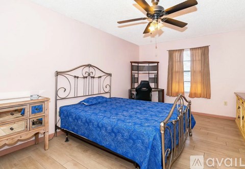 A bedroom with a blue bedspread and a ceiling fan.