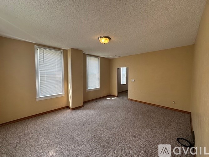 A room with carpeted floor, two windows, and a door.