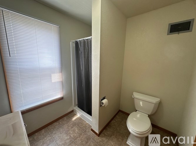 A bathroom with a toilet, a shower curtain, and a window with blinds.
