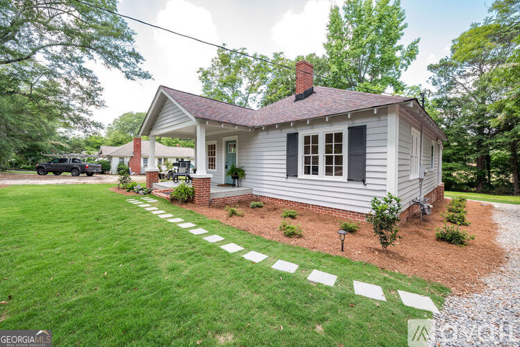 A small white house with a red brick chimney is surrounded by a green lawn and a gravel path.