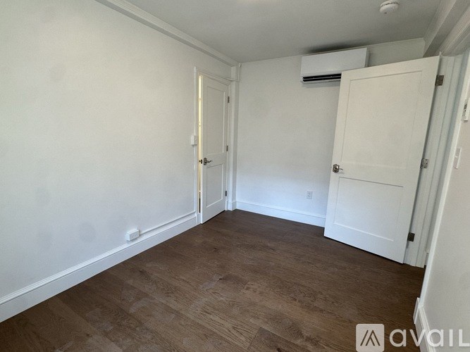 A room with white walls and wooden flooring, featuring two white doors.